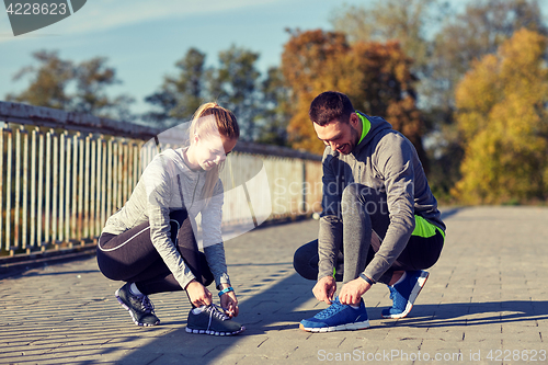 Image of smiling couple tying shoelaces outdoors