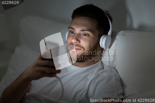 Image of man with smartphone and headphones in bed at night