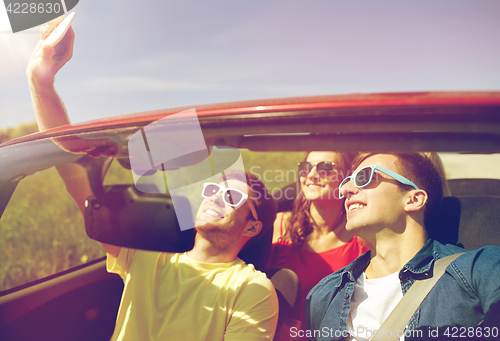 Image of friends driving in cabriolet car and taking selfie