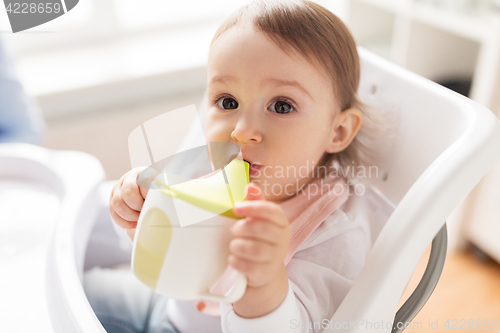 Image of baby drinking from spout cup in highchair at home