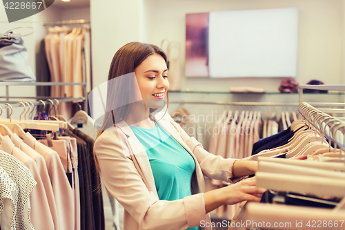 Image of happy young woman choosing clothes in mall