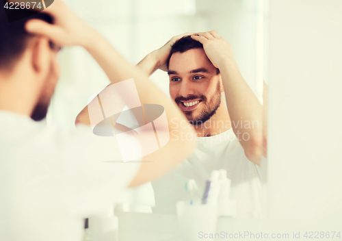 Image of happy young man looking to mirror at home bathroom