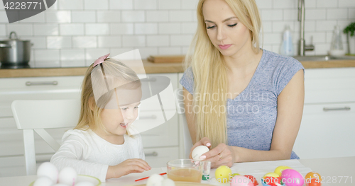 Image of Cheerful girl painting eggs with mother