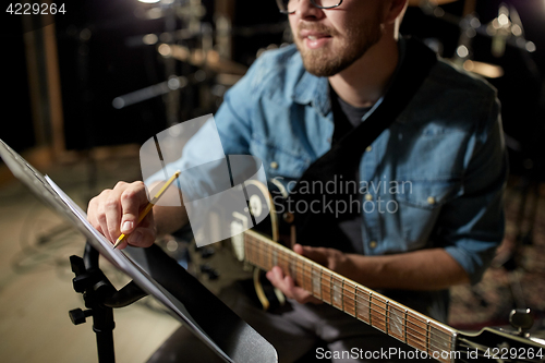 Image of man with guitar writing to music book at studio