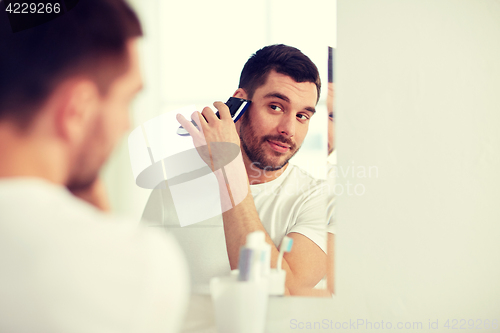 Image of man shaving beard with trimmer at bathroom