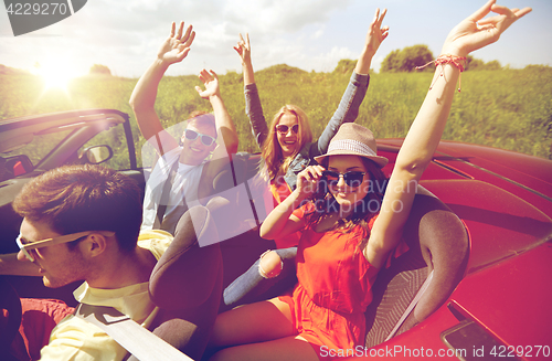 Image of happy friends driving in cabriolet car at country