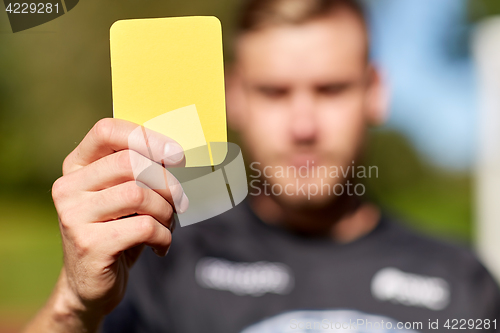 Image of referee on football field showing yellow card