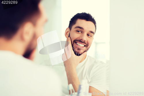 Image of happy young man looking to mirror at home bathroom