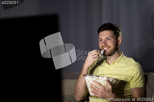 Image of happy man with popcorn watching tv at night