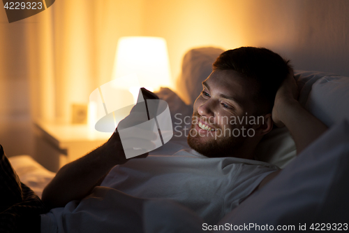 Image of happy young man with smartphone in bed at night