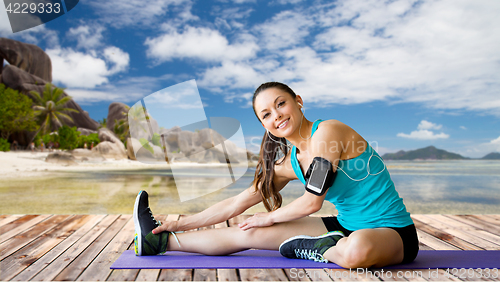 Image of woman with smartphone stretching leg on mat