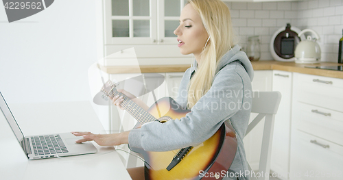 Image of Woman using laptop while playing guitar