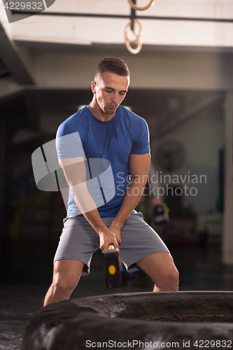 Image of man workout with hammer and tractor tire