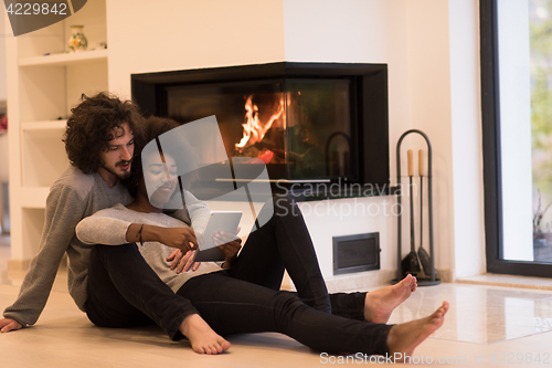 Image of multiethnic couple using tablet computer on the floor