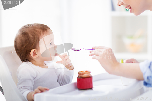 Image of happy mother feeding baby with puree at home