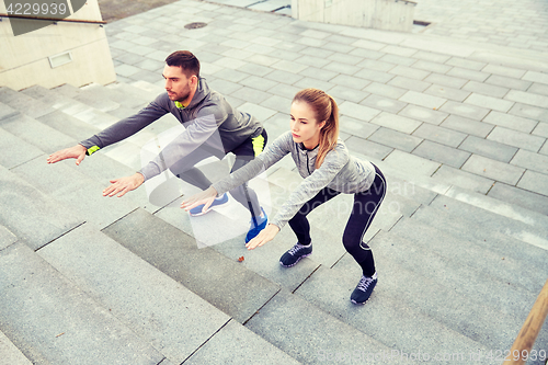 Image of couple doing squats on city street stairs