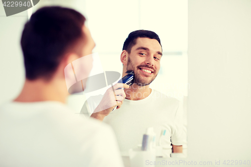 Image of man shaving beard with trimmer at bathroom