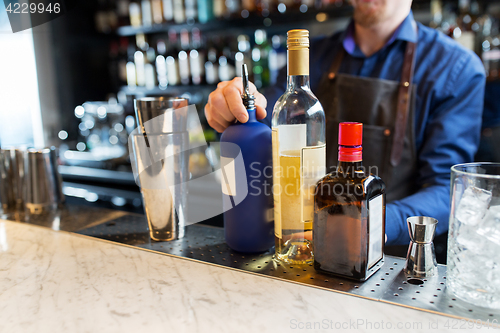 Image of barman with shaker, alcohol and jigger at bar