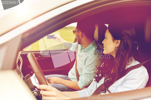 Image of happy couple in car taking selfie with smartphone