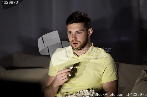 Image of man watching tv and eating popcorn at night