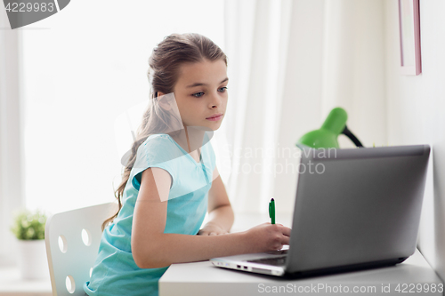 Image of girl with laptop writing to notebook at home
