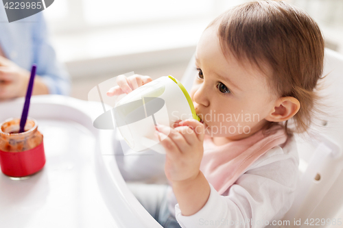 Image of baby drinking from spout cup in highchair at home