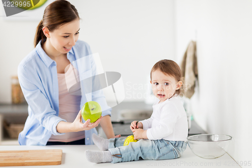 Image of mother giving green apple to baby at home kitchen