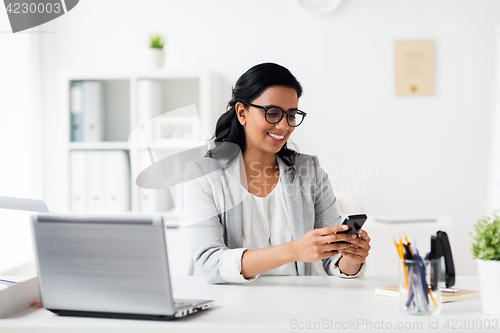 Image of businesswoman with smartphone and laptop at office