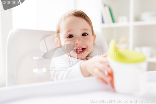 Image of baby drinking from spout cup in highchair at home