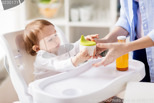 Image of mother giving spout cup with juice to baby at home