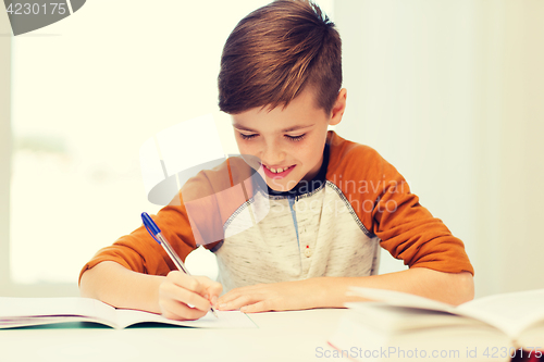 Image of smiling student boy writing to notebook at home