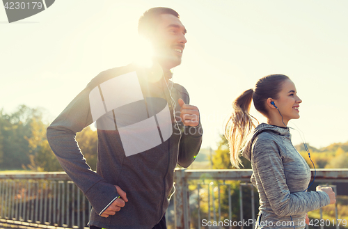 Image of happy couple with earphones running outdoors