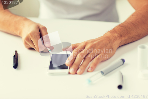 Image of close up of man with smartphone making blood test
