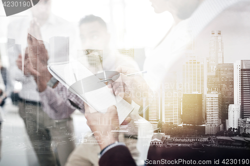 Image of business team and man writing to notepad at office