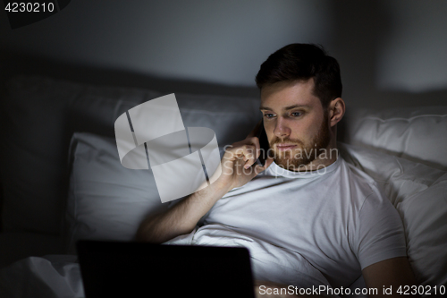 Image of man with laptop calling on smartphone at night