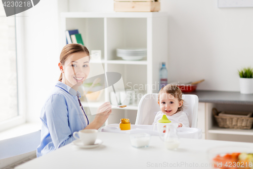 Image of happy mother feeding baby with puree at home