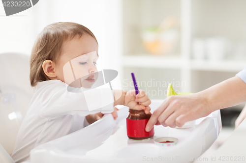 Image of baby with spoon eating puree from jar at home