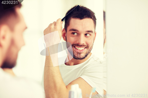 Image of happy man brushing hair  with comb at bathroom