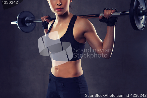 Image of young woman flexing muscles with barbell in gym