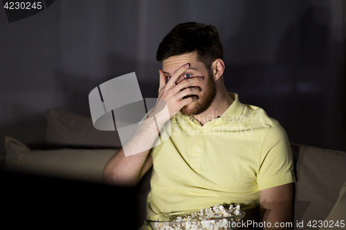 Image of scared man watching tv and eating popcorn at night