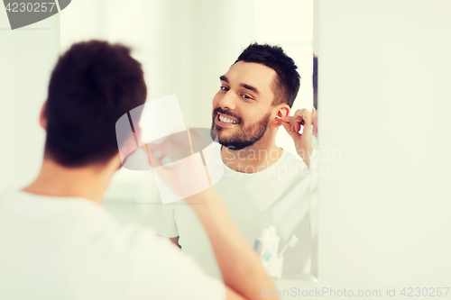 Image of man cleaning ear with cotton swab at bathroom