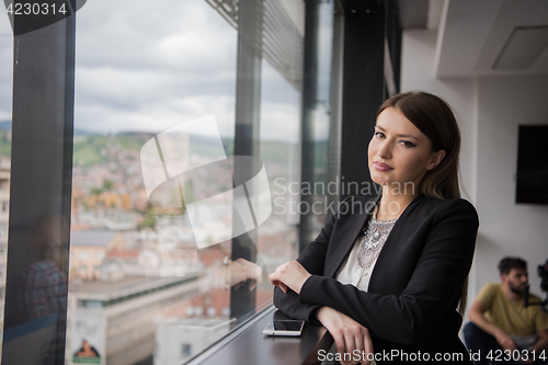 Image of Elegant Woman Using Mobile Phone by window in office building