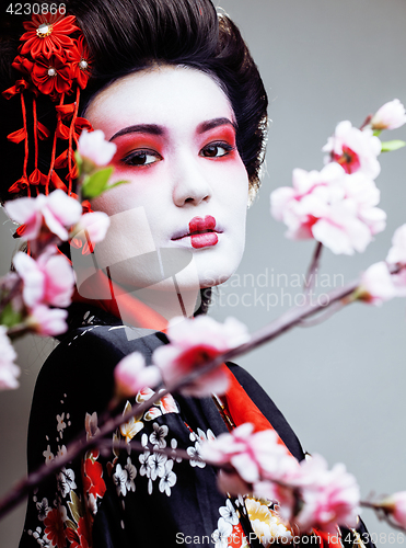 Image of young pretty geisha in black kimono among sakura, asian ethno close up concept