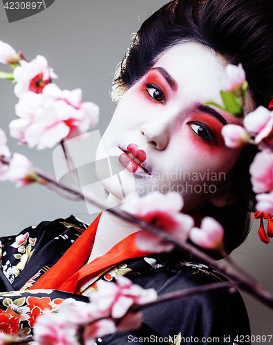 Image of young pretty geisha in black kimono among sakura, asian ethno close up