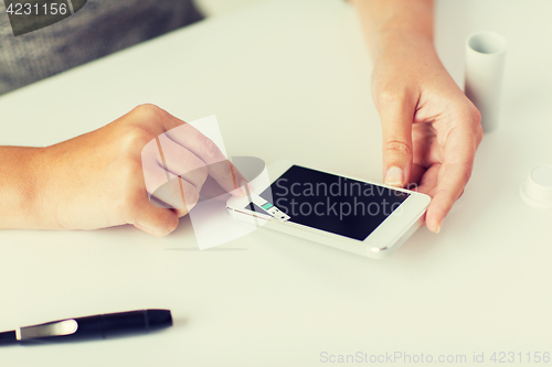 Image of close up of woman with smartphone doing blood test