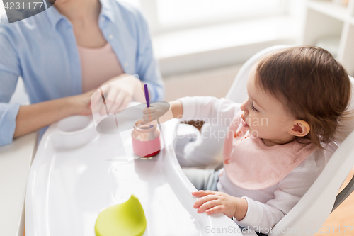 Image of baby girl with spoon eating puree from jar at home