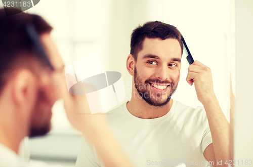 Image of happy man brushing hair  with comb at bathroom