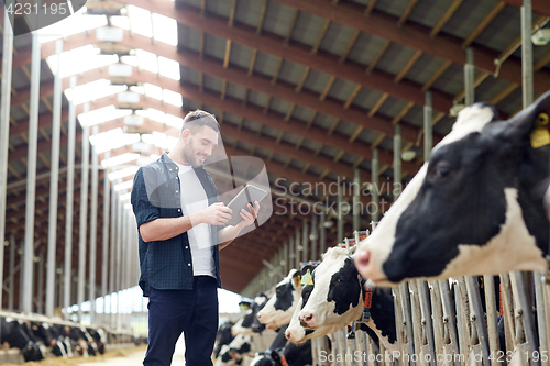 Image of young man with tablet pc and cows on dairy farm