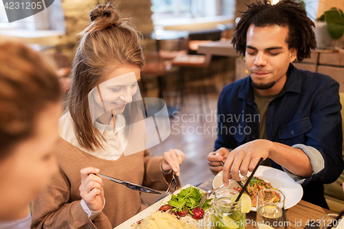 Image of happy friends eating and drinking at restaurant