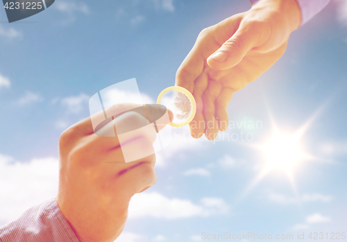 Image of close up of male gay couple hands giving condom